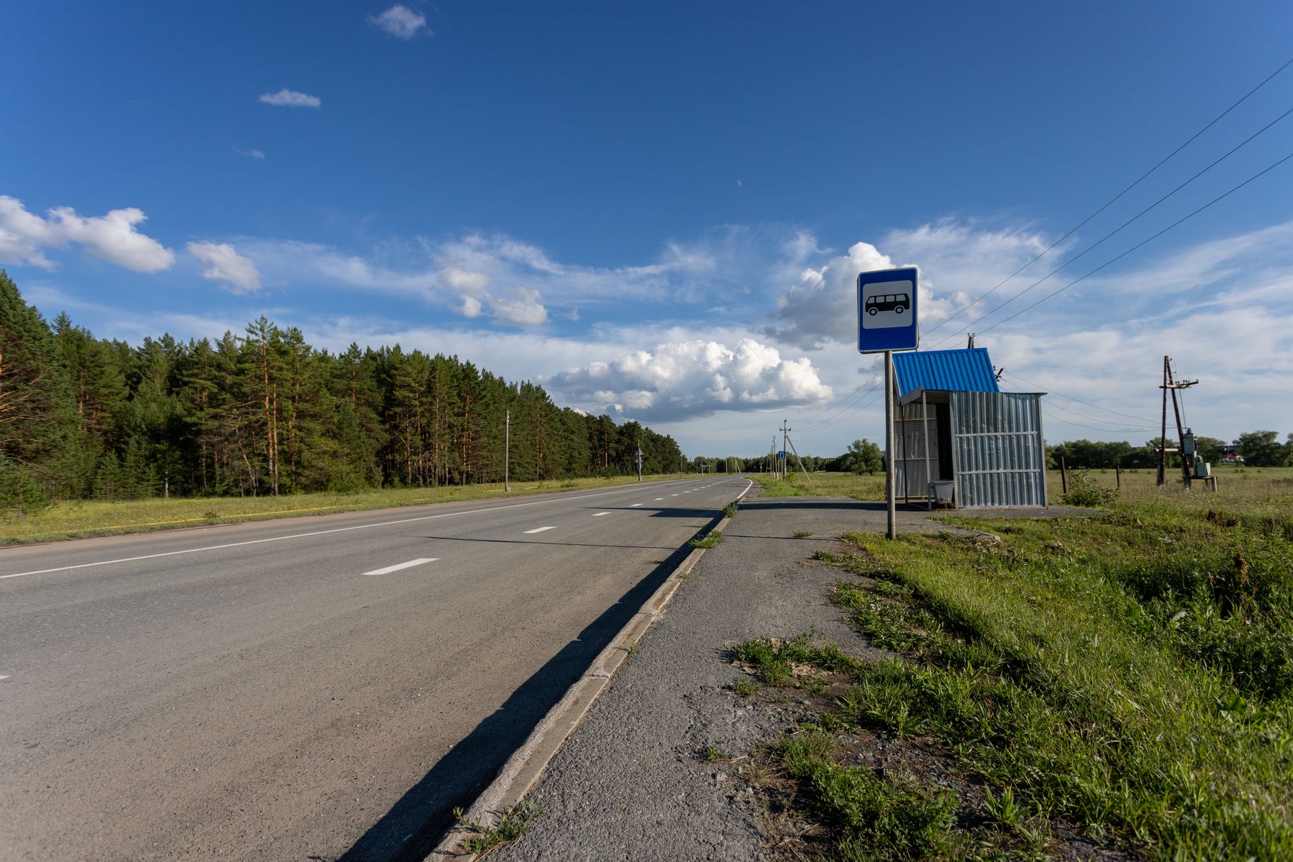 A quiet rural road with an empty bus stop under a clear blue sky in Sinitsyna, Russia.