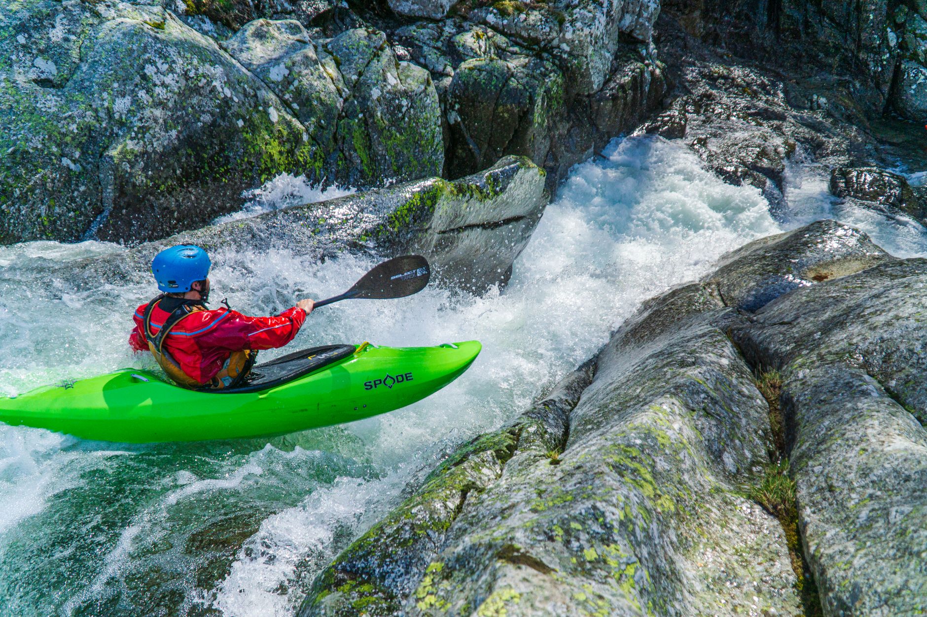 An adventurous kayaker in a bright green kayak tackles thrilling whitewater rapids in Occitanie, France.