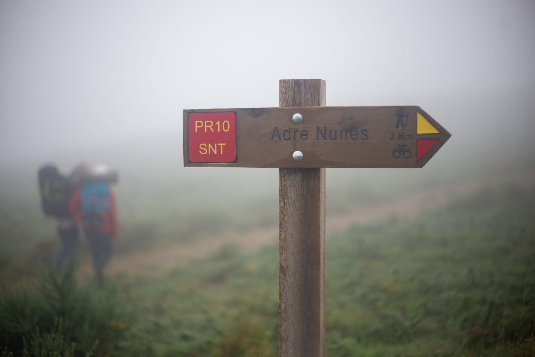 Trail sign marking the path to Adre Nunes in Portugal, captured on a foggy day.