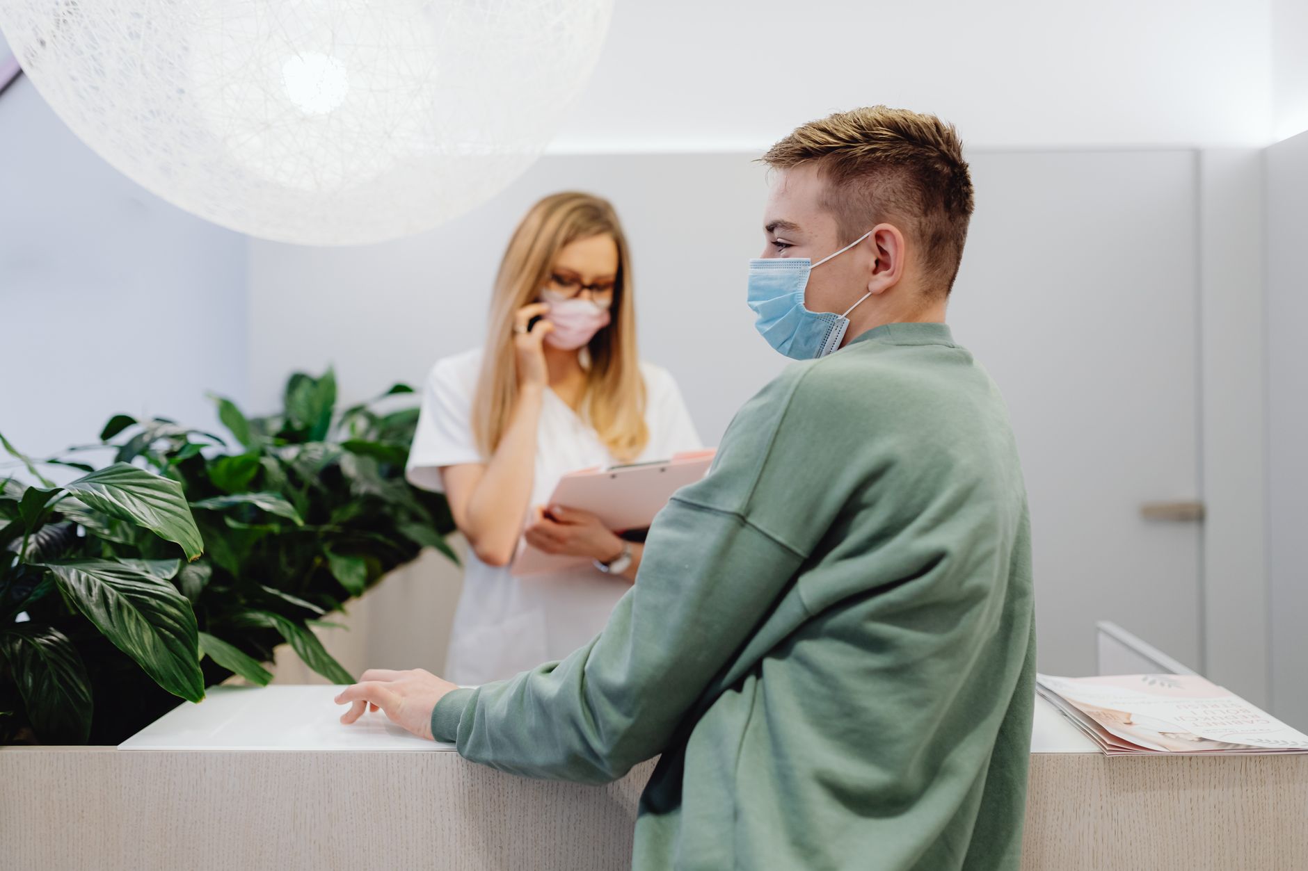 Un patient et un réceptionniste dans une clinique portant des masques, garantissant la sécurité sanitaire.