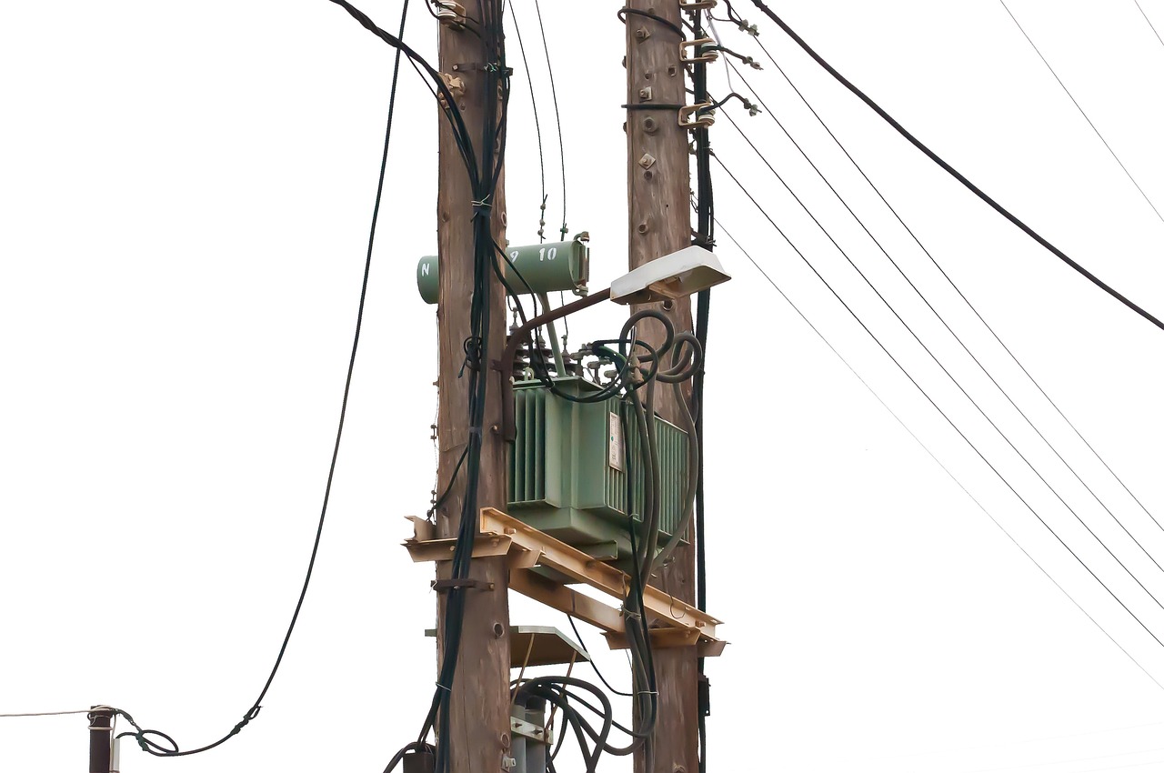 Poteau en bois portant un transformateur et plusieurs câbles électriques, photographié sur fond blanc